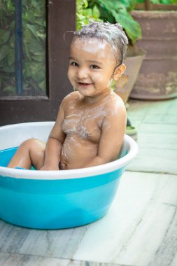 Yeni yürümeye başlayan çocuk, dışarıda küvette şampuan ve sabunla banyo yapmayı eşsiz bir bakış açısıyla seviyor.