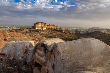 Renkli şehir evleri ve akşam vakti gökyüzü dramatik bulutlu olan antik tarihi kale Mehrangarh Kalesi Jodhpur Rajasthan Hindistan 'da çekilmiştir..