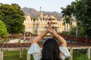 young girl praying at ancient unique temple with bright sky at day from back angle image is taken at ranakpur jain temple rajasthan india. clipart