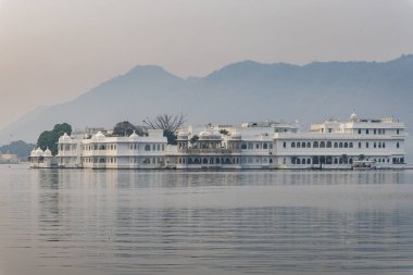 El değmemiş göldeki sanatsal saray mimarisi ve sabah görüntülerindeki sisli dağ arkaplanı Udaipur Rajasthan Hindistan 'da çekilmiştir..