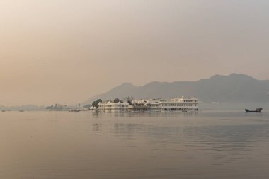El değmemiş göldeki sanatsal saray mimarisi ve sabah görüntülerindeki sisli dağ arkaplanı Udaipur Rajasthan Hindistan 'da çekilmiştir..