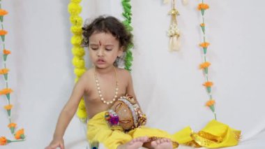Hindu tanrısı Kirshna gibi giyinmiş, beyaz arka planı olan küçük bir çocuk.