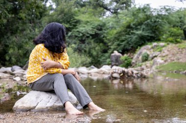 Isolated Girl Sitting Alone on Stone at Calm Lake Shore in the Morning clipart