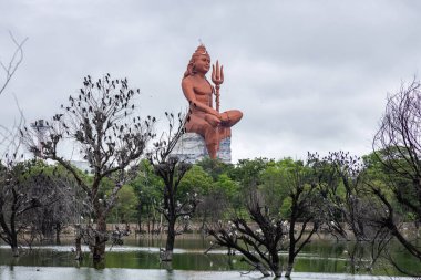 Isolated Statue of holy Hindu Lord Shiva in Meditation Posture with dramatic sky and pristine lake clipart