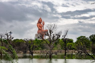 Kutsal Hindu Lord Shiva 'nın izole edilmiş heykeli dramatik gökyüzü ve el değmemiş gölle meditasyon içinde.