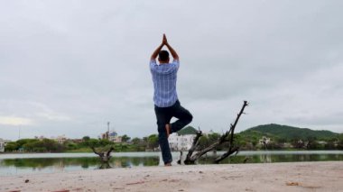 Genç adam meditasyon yapıyor ve yoga yapıyor... el değmemiş sakin göl kenarında... sabahları dramatik gökyüzü ile...