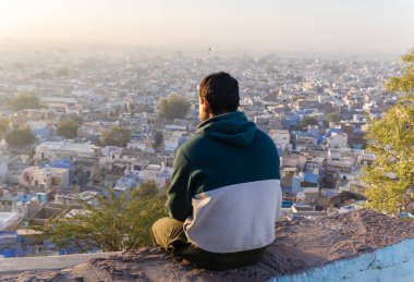 Genç adam sabah dağın tepesinden şehir manzarasına bakıyor.