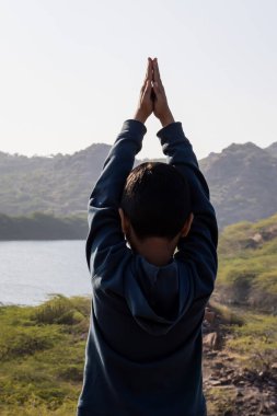 İzole edilmiş genç bir çocuk, sabahları göl manzaralı dağın tepesinde yoga pratiği yapıyor.
