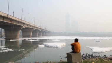 Contaminated River 'daki zehirli köpüğe bakan izole bir adam ile Bridge Foggy City' nin yakınlarında sabah videosu yamuna River Okhla Barrage Delhi 'de çekildi..