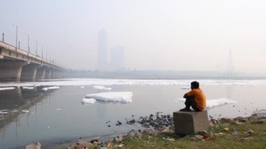 Contaminated River 'daki zehirli köpüğe bakan izole bir adam ile Bridge Foggy City' nin yakınlarında sabah videosu yamuna River Okhla Barrage Delhi 'de çekildi..