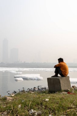 Sabahleyin Contaminated River 'daki zehirli köpüğe bakan yalnız bir adam ile Foggy City Köprüsü yakınındaki yamuna Nehri Okhla Barrage Delhi' de çekiliyor..
