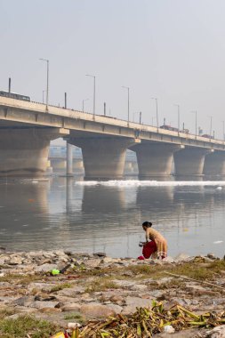 Isolated women doing holy rituals at Polluted River with Toxic Foam at misty Morning image is taken at yamuna river okhla barrage delhi india. clipart