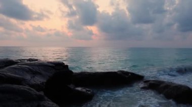 Deniz sahili, şafak vakti gökyüzü dramatik bir şekilde aydınlanırken düz açılı video Kala Pathar Sahili 'nde Andaman ve Nicobar Adaları' nı kasıp kavuruyor..