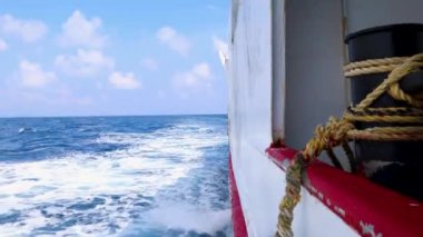 Sakin deniz ufku, gemi su izleri ve parlak mavi gökyüzünün altında demirleyen ipler.