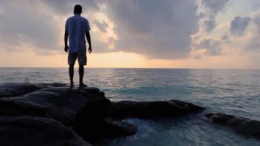 Kala Pathar Sahili 'nde Andaman ve Nicobar Adaları' nda izole edilmiş genç bir adam şafak vakti dramatik gökyüzü ile deniz ufkuna bakıyor..