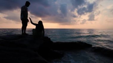 Kala Pathar Plajı 'nda Andaman ve Nicobar Adaları' nda el ele tutuşan ve kayalık kıyılarda yardım eden evli bir çift ve deniz ufku ve dramatik gökyüzü videosu çekildi..
