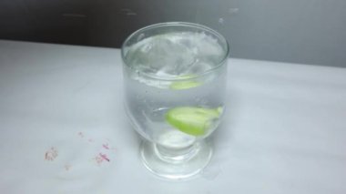 Stüdyo ışığında taze zerdeçal, limon, salatalık ve zencefil dilimli bir bardak su.