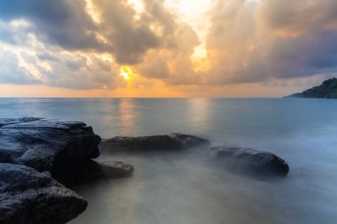 Gün doğumu dramatik gökyüzü deniz ufkunda şafak vakti kayalık sahilden uzun pozlu çekim