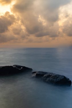 sunrise dramatic sky over sea horizon from rocky shore at dawn long exposure shot clipart