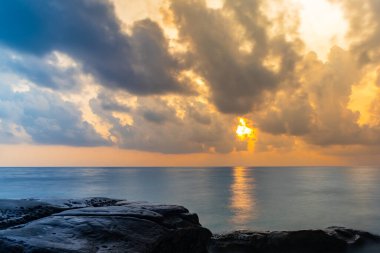 Gün doğumu dramatik gökyüzü deniz ufkunda şafak vakti kayalık sahilden uzun pozlu çekim