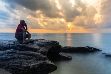 Ayrı yaşayan yaşlı adam konuşuyor. Uzun pozlama bulanıklığı, gün doğumu gökyüzü ve deniz ufku.