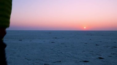 Beyaz çölde yürüyen genç adam şafak vakti turuncu gökyüzü dramatik bir şekilde farklı açılardan çekiliyor. Video Dhordo Kutch White Rann Gujrat Hindistan 'da çekiliyor..