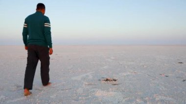 Genç adam, beyaz tuz çölünde yalın mavi gökyüzü ile yürüyordu. Düz açılı video, Dhordo Kutch White Rann Gujrat Hindistan 'da çekildi..