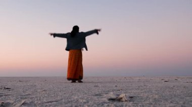 Genç kız, uzak beyaz tuz çölünde turuncu gökyüzü ile zafer işareti gösteriyor. Video, Dhordo Kutch White Rann Gujrat Hindistan 'da çekiliyor..