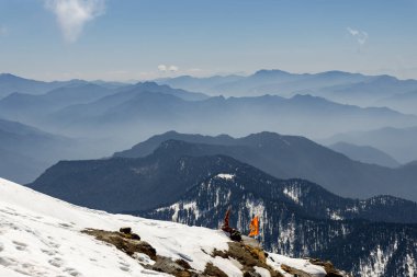 Bulutlu mavi gökyüzü altında kutsal bayrağı olan kar örtüsü dağ manzarası Chandrashila yürüyüşü tungnath chopta uttarakhand Hindistan 'da çekilmiştir..