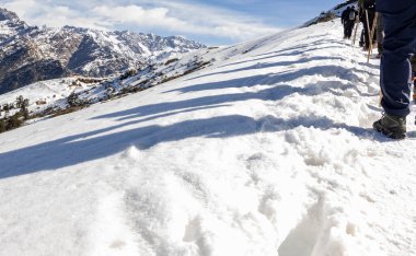 Yürüyüş grubunun gölgesi, sabah taze beyaz kar üzerinde yürürken Chopta Tungnath Himalayalar 'da çekilir Chandrashila Dağı' nda..