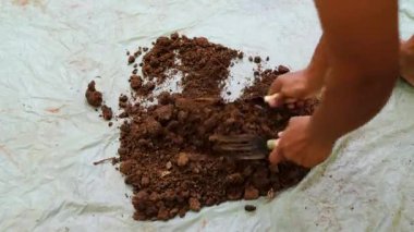 Bahçıvan, açık havada plastik çarşafta inek gübresi karıştırıyor.
