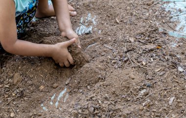 Çocuğun eli dışarıda plastik çarşafta bahçe toprağıyla oynuyor.