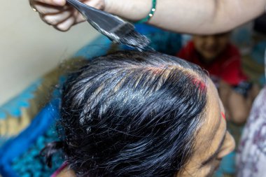 Yaşlı bir kadın ev ışıklandırmasının altında saç boyuyor.