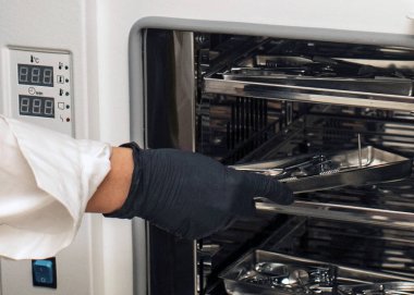 Bir eldiven uzmanı sterilizatöre manikür ve pedikür aletleri yükler. Kozmetik prosedürleri sırasında hijyen ve güvenlik