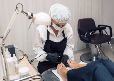 Güzellik uzmanı eldiven ve koruyucu maske bir güzellik salonunda nalbur pedikür yapar. Profesyonel ekipman ve kesicilerle ayak tedavisi. Ayak bakımı, hijyen. Yüz görünürde yok.