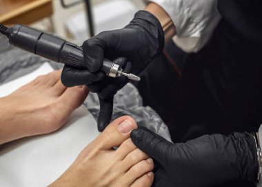 Usta bir güzellik salonunda nalbur pedikür yapıyor. Profesyonel ekipman ve kesicilerin yardımıyla ayağın incelenmesi. Ayak bakımı, hijyen, güzellik tedavisi.