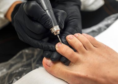 Usta bir güzellik salonunda nalbur pedikür yapıyor. Profesyonel ekipman ve kesicilerin yardımıyla ayağın incelenmesi. Ayak bakımı, hijyen, güzellik tedavisi.