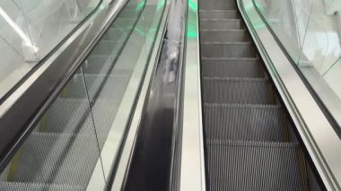 Modern yürüyen merdiven yukarı çıkıyor, yanında da aşağı doğru yürüyen bir yürüyen merdiven var. Parlak ışıklandırma parlak camlara ve metal yüzeylere yansıyor. Kentsel ulaşım kavramı