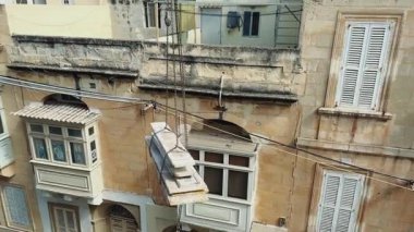 Dar bir caddedeki bir konut binasında yenileme çalışmaları: Zincirler ve vinçle alt kattan üst kata ahşap kalasları kaldırmak