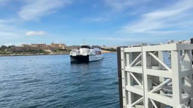Malta toplu taşıma feribotu yolcuları Vallettas rıhtımında üst güvertede. Güneşli bir gün, mavi deniz, metal yapılar ve uygun altyapı..