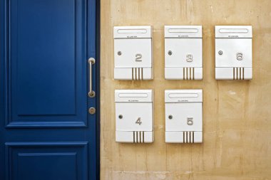 Kompozisyonda kentsel minimalizm: Büyük metal saplı koyu mavi bir kapının yanında, eski sarı duvarda 