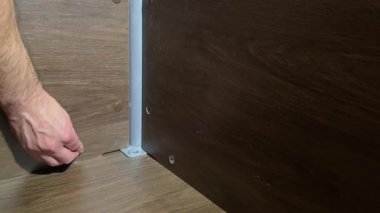 Tahta bir masanın köşesindeki cıvata deliklerine plastik kapaklar takan bir elin yakın çekimi. Mobilya donanımını korumak ve görünüşünü iyileştirmek..