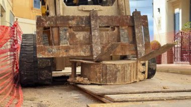 Paslı forklift, yıpranmış metal çatallar ve inşaat alanında ağır bir karşı ağırlık. Endüstriyel makinelerin güvenlik bariyerleriyle kentsel çalışma sahasına yakın görüntüsü.