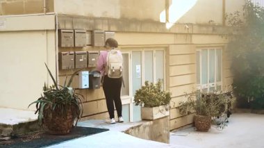 San Giljan, Malta - 04.09.2025: Öğrenci çalışmaları: Güneşli bir günde, açık bir bölgedeki posta kutularına pembe ceketli genç bir kadın postacı