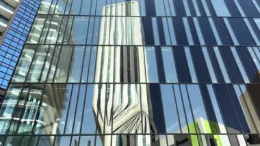 Çağdaş gökdelen hatlarını yansıtan ve çarpıtan parlak cam paneller berrak mavi gökyüzüne karşı soyut kentsel şekiller oluşturuyor..