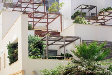 Ahşap pergolalı ve yeşillikli modern çok katlı bina. Seçici odak, yumuşak bir ön plan derinliği ve detayı ile teraslı mimarinin temiz çizgilerini vurgular.