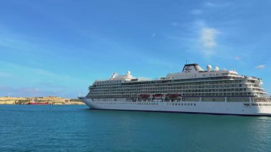 Valletta, Malta - 02.28.2025: Viking yolcu gemisi açık mavi gökyüzünün altından yelken açtı. Yolcular lüks yolcu gemisi okyanus yolculuğuna başlarken manzaranın tadını çıkarıyorlar..
