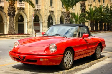 Şehir caddesinde palmiye ağaçları ve eski binalarla park edilmiş klasik kırmızı bir araba. Farlara ve ön tarafa odaklan. Sıcak tonlar ve bulanık arkaplan yumuşak bir alan etkisi yaratır