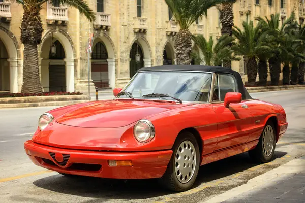 Şehir caddesinde palmiye ağaçları ve eski binalarla park edilmiş klasik kırmızı bir araba. Farlara ve ön tarafa odaklan. Sıcak tonlar ve bulanık arkaplan yumuşak bir alan etkisi yaratır