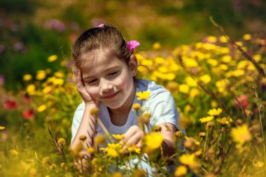 Sarı kır çiçekleriyle çevrili, çiçek açan bir çayırda güneşli bir bahar gününün tadını çıkaran mutlu genç bir kız. Huzurlu gülüşü ve doğal görünüşü neşe, masumiyet ve doğa sevgisini ifade ediyor..